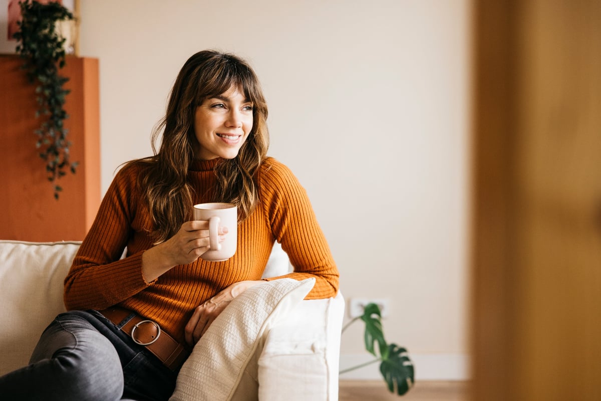 Young adult woman smiling and relaxing at home with a coffee mug
